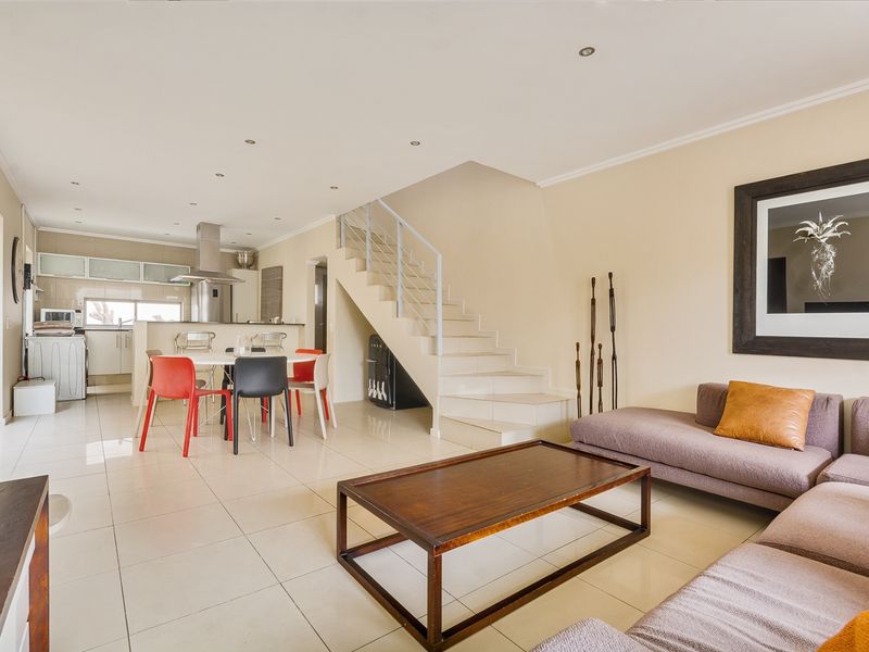 Spacious open-plan living and dining area featuring tiled floors, recessed lighting, and a modern staircase, seamlessly flowing into the kitchen space.