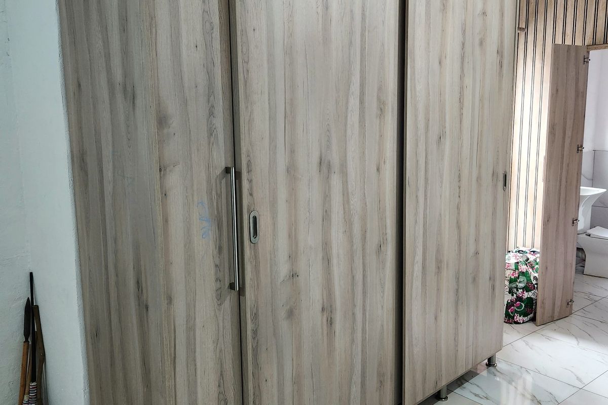 A bedroom featuring a large, modern wood-grain built-in wardrobe with sliding doors and light-colored floor tiles.