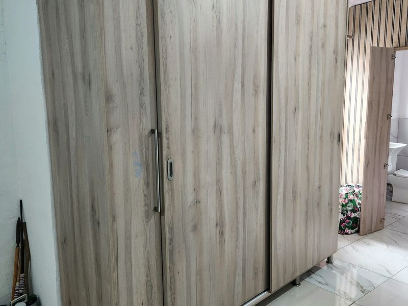 A bedroom featuring a large, modern wood-grain built-in wardrobe with sliding doors and light-colored floor tiles.