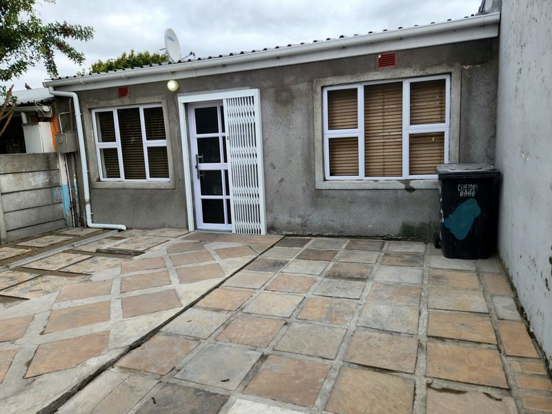 Rear exterior view featuring a paved patio area, security gate, and weathered wall finish, providing a functional outdoor space.