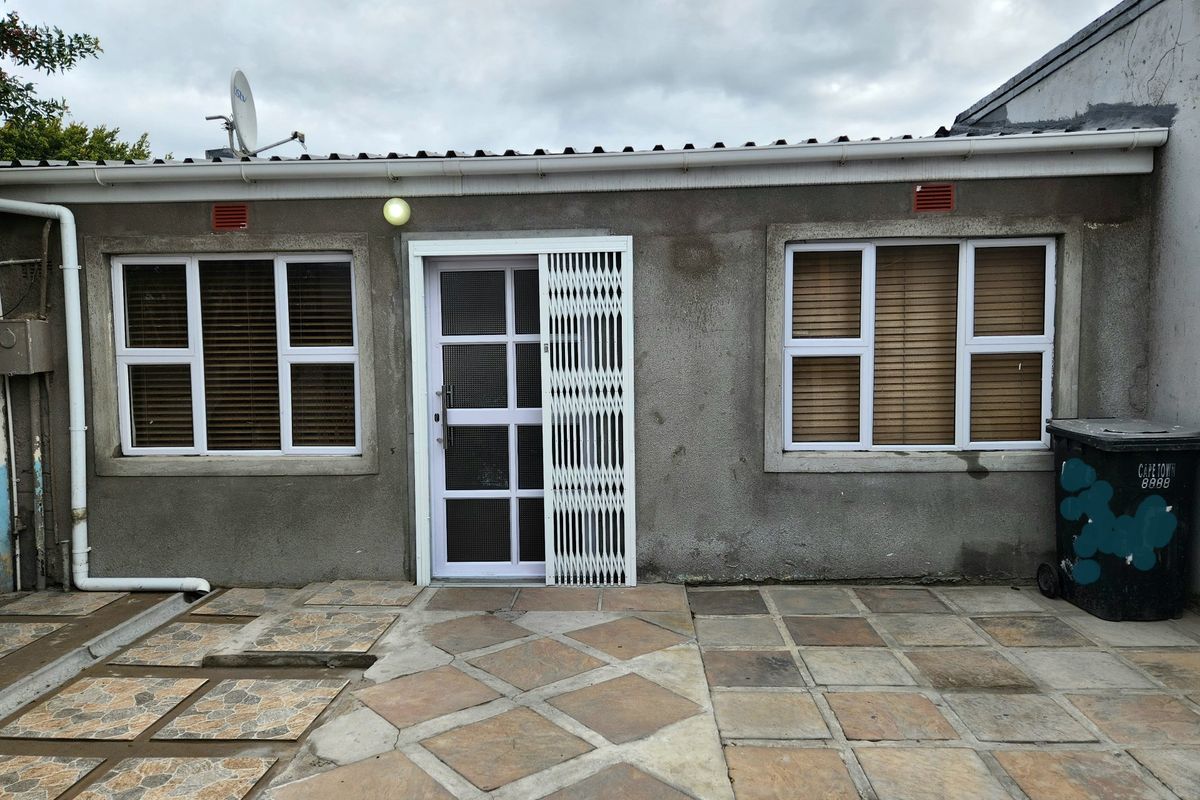 Rear exterior view of the property featuring a paved patio area, security gate, and aluminium window frames.