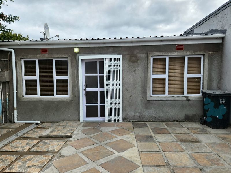 Rear exterior view of the property featuring a paved patio area, security gate, and aluminium window frames.