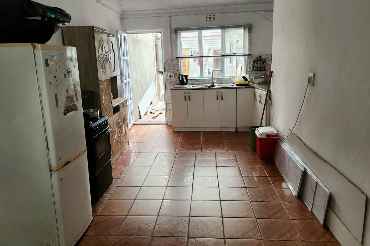 A functional kitchen featuring tiled flooring, white cabinetry, and a stainless steel sink, with direct access to an outdoor area.