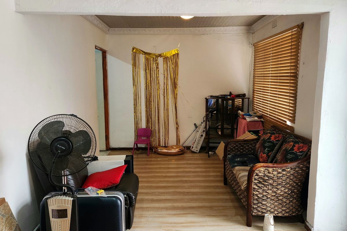 A living room area featuring laminate flooring, tiled transition, and venetian blinds, requiring cosmetic updates to improve the overall aesthetic.