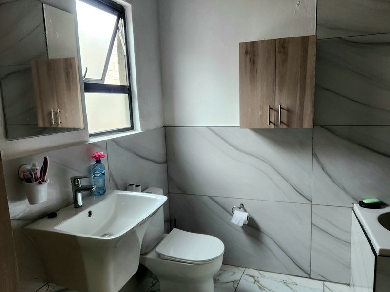 A compact bathroom featuring modern marble-look wall and floor tiles, a wall-mounted basin, and a wooden wall-mounted storage cabinet.