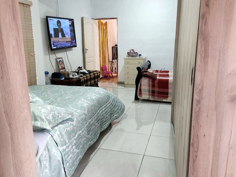 Spacious bedroom featuring tiled flooring, crown molding, and a built-in wardrobe, offering a functional layout with direct access to an adjoining room.