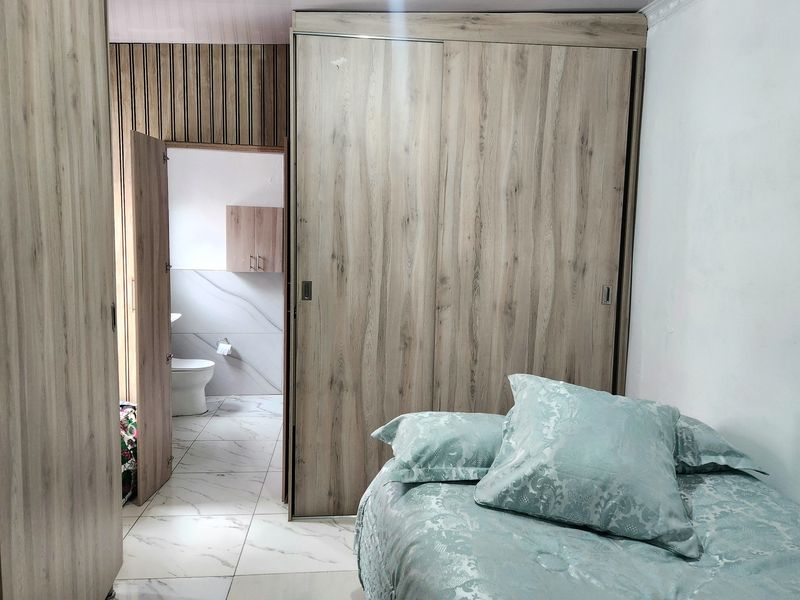 Bedroom featuring light wood-grain built-in wardrobes, tiled flooring, and direct access to an en-suite bathroom with modern finishes.