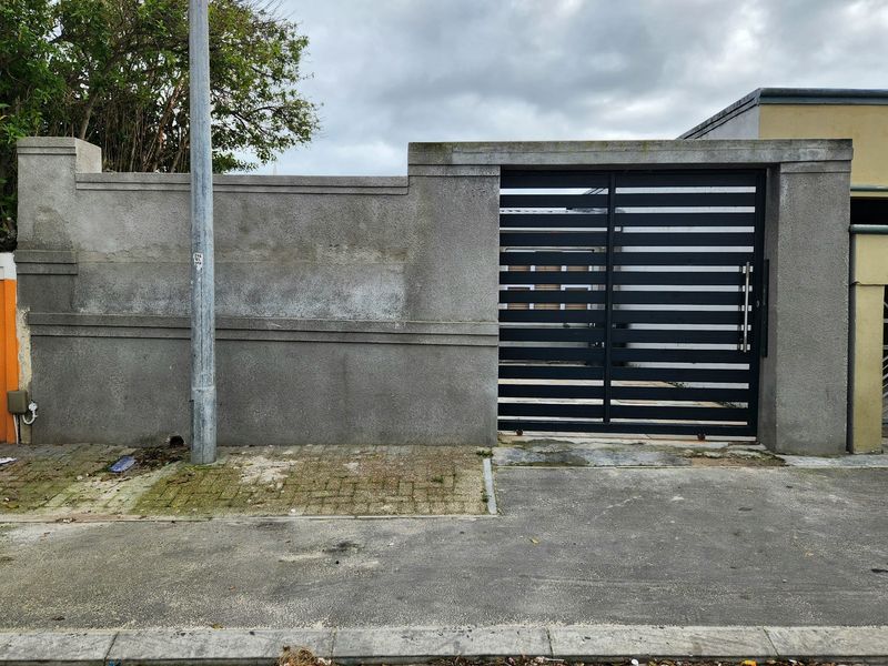 Front boundary wall with a modern black metal gate and paved entrance area.