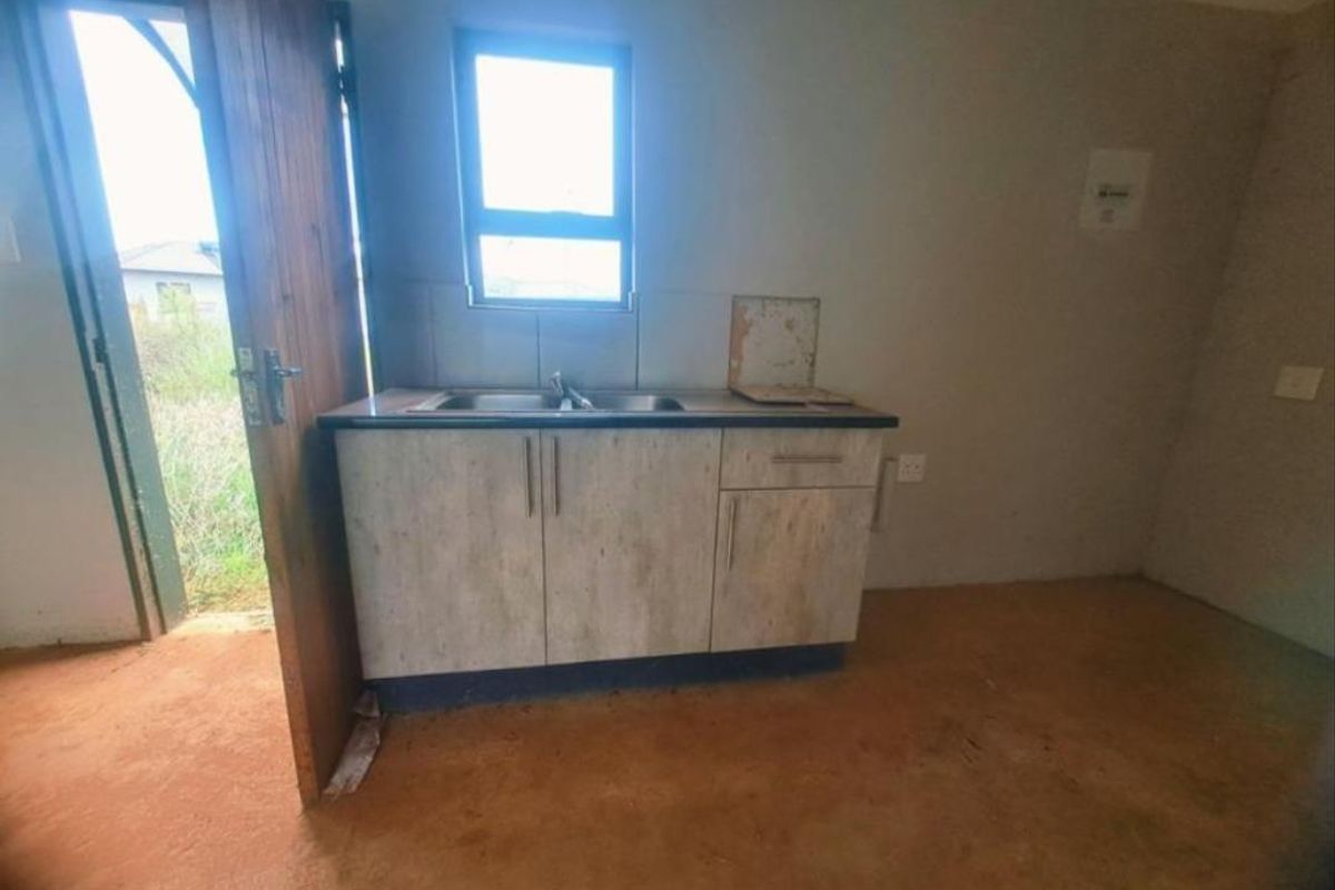 A basic, unfinished kitchen area featuring a small cabinet unit with a stainless steel sink and direct access to the exterior.