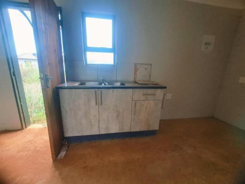 A basic, unfinished kitchen area featuring a small cabinet unit with a stainless steel sink and direct access to the exterior.