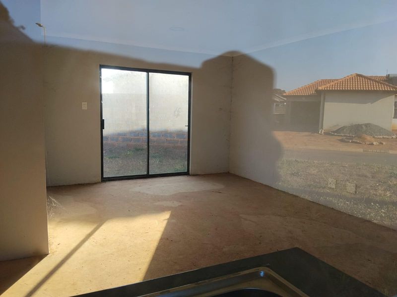 An empty open-plan living area featuring a sliding glass door and a kitchen sink area, currently in an unfinished state.