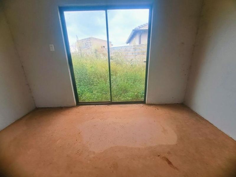 An unfinished bedroom space featuring a sliding glass door with views of the rear yard, requiring flooring and wall finishes.