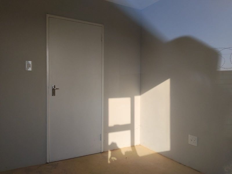 An empty bedroom featuring neutral painted walls, a standard internal door, and basic electrical fixtures, ready for personalization.