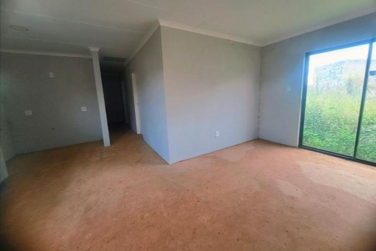 An empty, unfinished living area featuring a large sliding glass door and neutral wall finishes, ready for flooring and final interior touches.