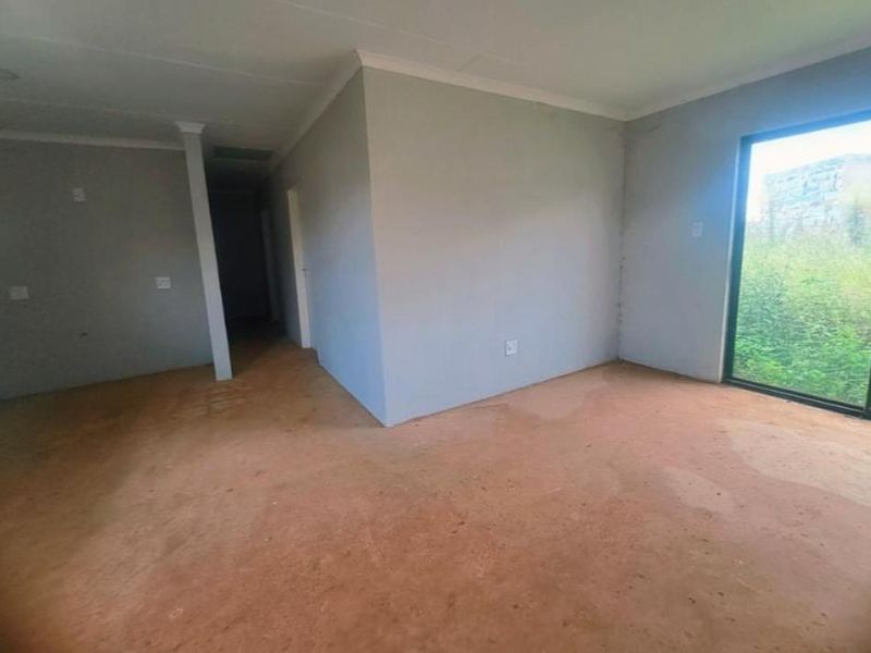 An empty, unfinished living area featuring a large sliding glass door and neutral wall finishes, ready for flooring and final interior touches.