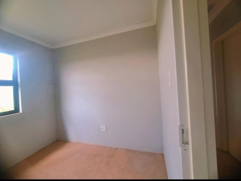 An empty bedroom featuring neutral walls, a window, and an electrical outlet, ready for customization.