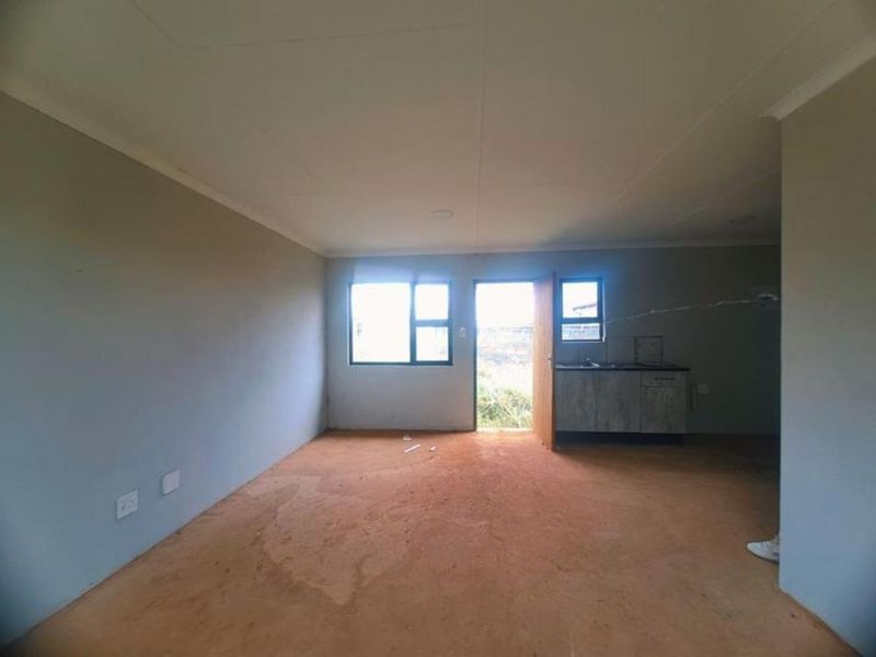 An open-plan living and kitchen area featuring basic cabinetry, a sink, and unfinished flooring, offering a blank canvas for renovation.