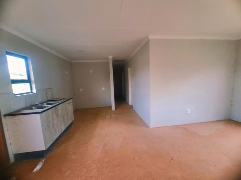 An empty open-plan living and kitchen area featuring basic cabinetry, a double sink, and unfinished flooring, offering a blank canvas for renovation.