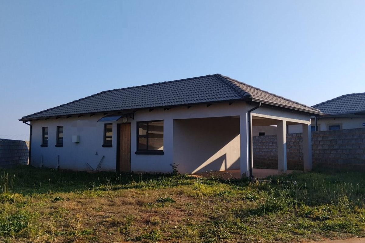 Rear view of a single-story house featuring a tiled roof, covered patio area, and surrounding concrete block boundary walls on an unlandscaped plot.