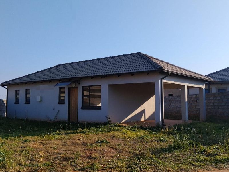 Rear view of a single-story house featuring a tiled roof, covered patio area, and surrounding concrete block boundary walls on an unlandscaped plot.