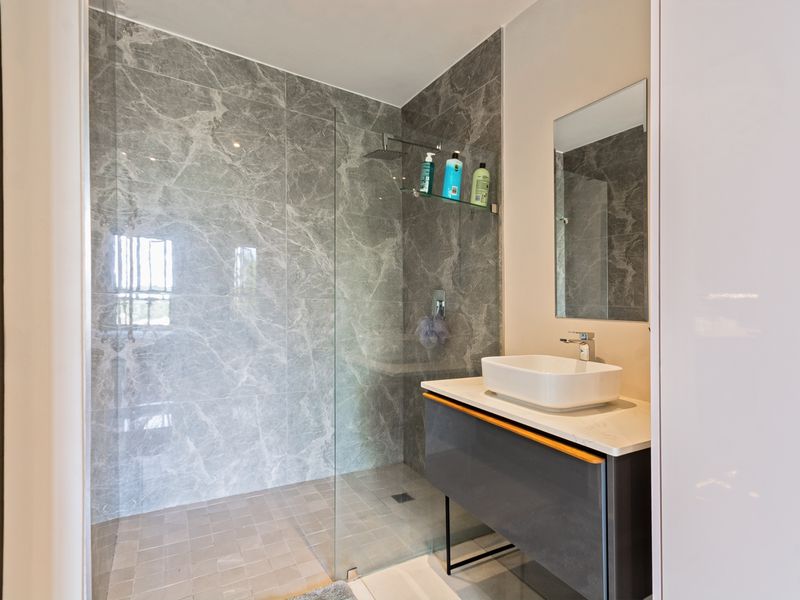 Modern bathroom featuring a walk-in shower with marble-effect tiling, a sleek vanity unit with a vessel sink, and a wall-mounted mirror.