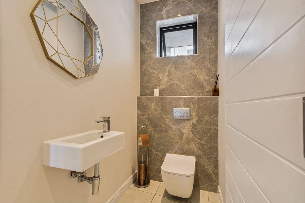 Modern guest bathroom featuring a wall-hung toilet with concealed cistern, marble-look feature tiling, and a sleek wall-mounted basin.