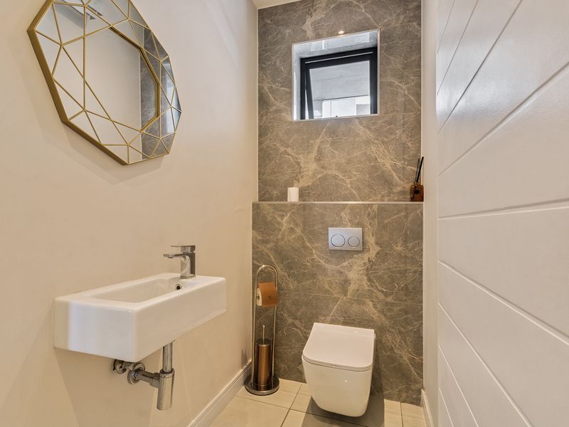 Modern guest bathroom featuring a wall-hung toilet with concealed cistern, marble-look feature tiling, and a sleek wall-mounted basin.