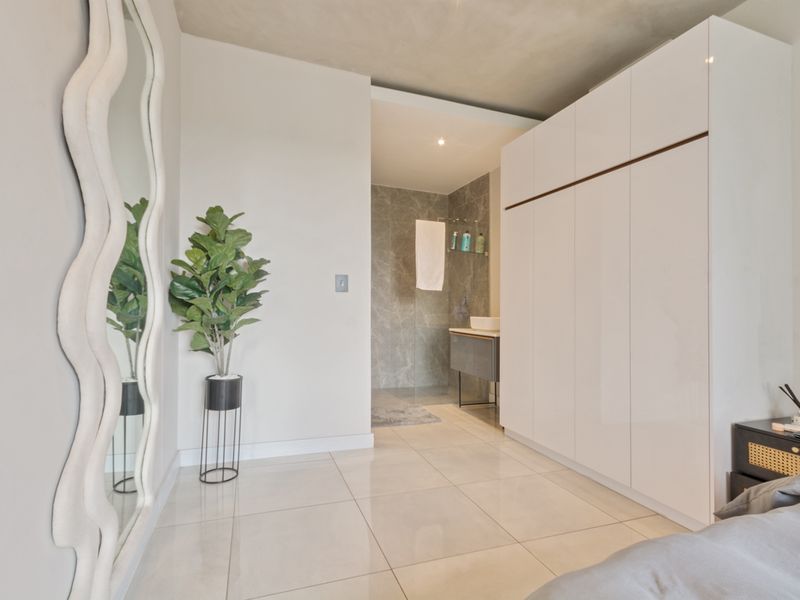 Modern bedroom featuring sleek built-in cupboards, polished tile flooring, and a seamless transition into an en-suite bathroom area.