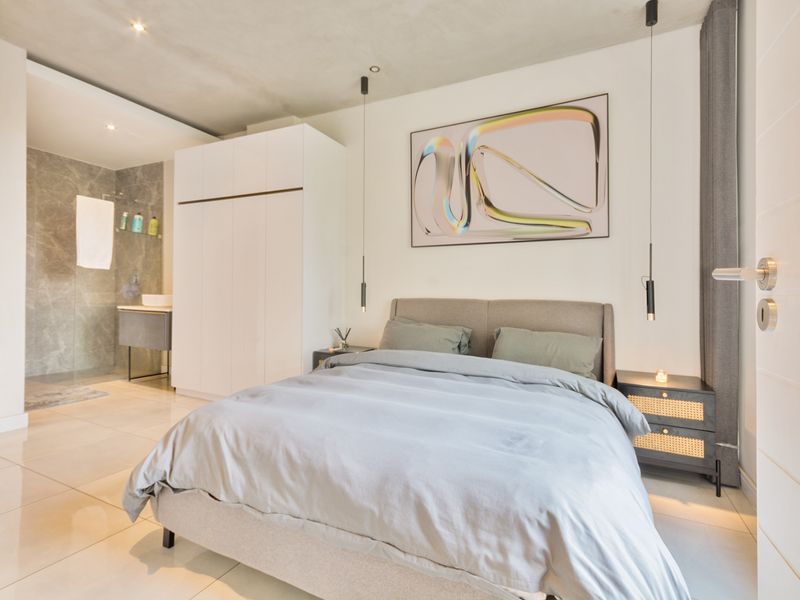 Modern bedroom featuring tiled flooring, built-in wardrobe, and an open-plan en-suite bathroom with contemporary finishes and recessed lighting.