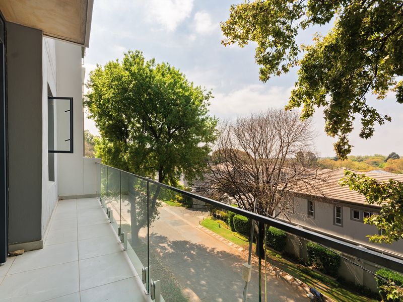 A clean, modern balcony featuring a glass balustrade and tiled flooring, offering an elevated view of the surrounding neighborhood and mature trees.