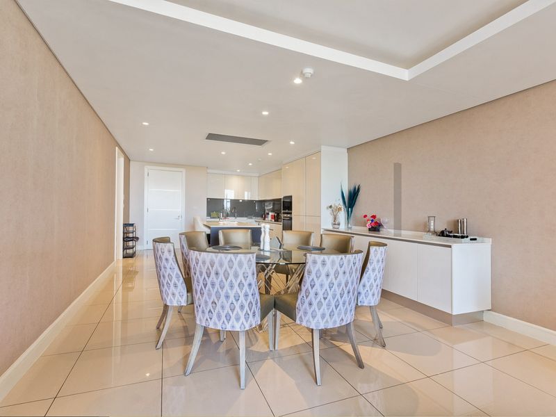 Spacious open-plan dining and kitchen area featuring modern cabinetry, integrated appliances, recessed ceiling lighting, and polished porcelain floor tiles.