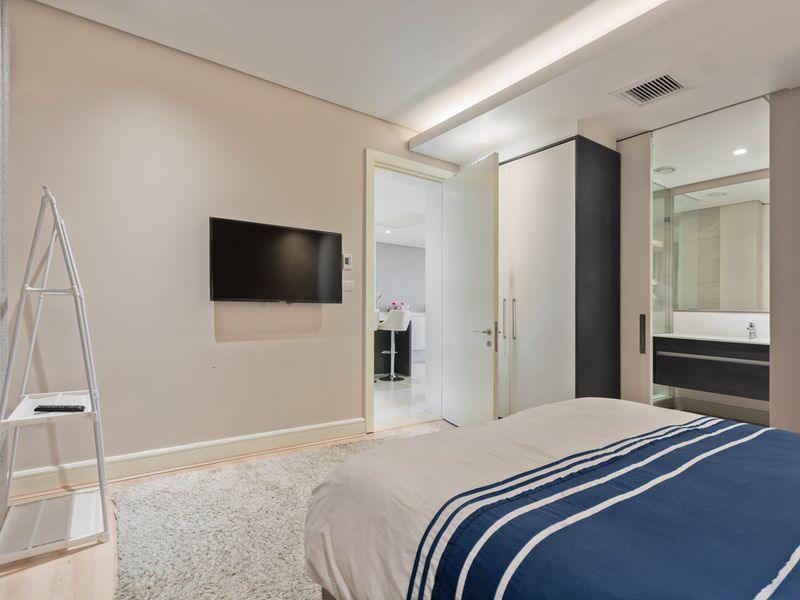 A modern bedroom featuring built-in wardrobes, recessed ceiling lighting, and an integrated en-suite bathroom with contemporary finishes.