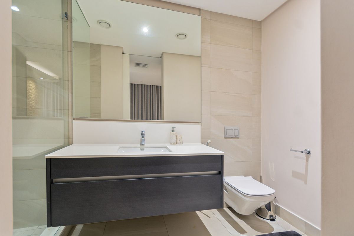 Modern bathroom featuring a sleek wall-mounted vanity, integrated basin, large mirror, wall-hung toilet with concealed cistern, and a glass-enclosed shower.