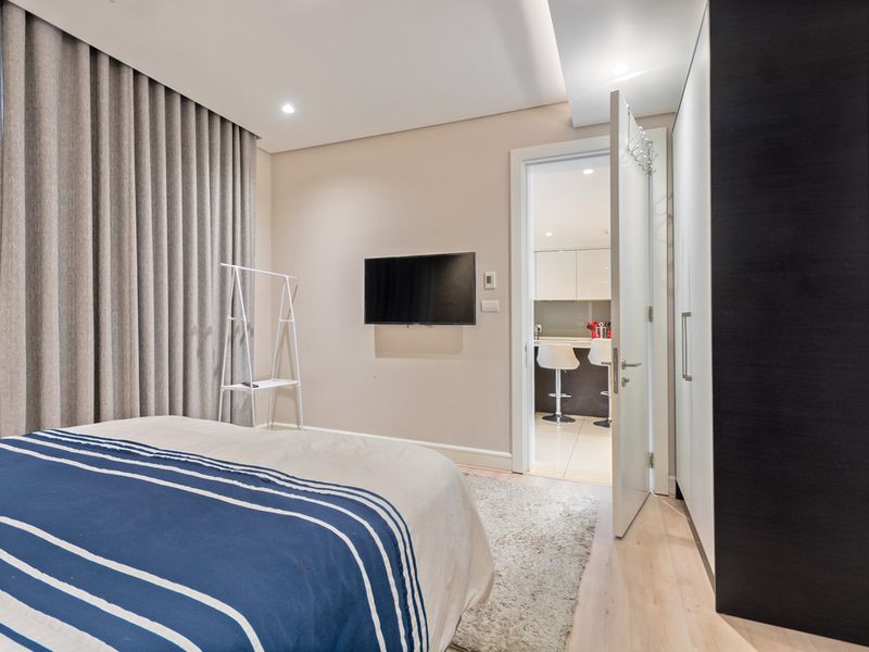 A well-maintained bedroom featuring laminate flooring, recessed lighting, and a built-in wardrobe, with a direct view into the adjacent kitchen area.