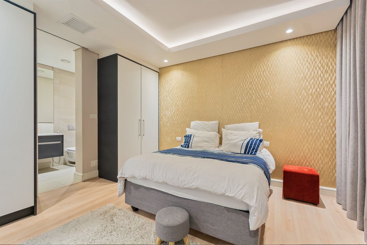 Modern bedroom featuring a textured gold feature wall, built-in wardrobe, recessed ceiling lighting, and direct access to an en-suite bathroom.