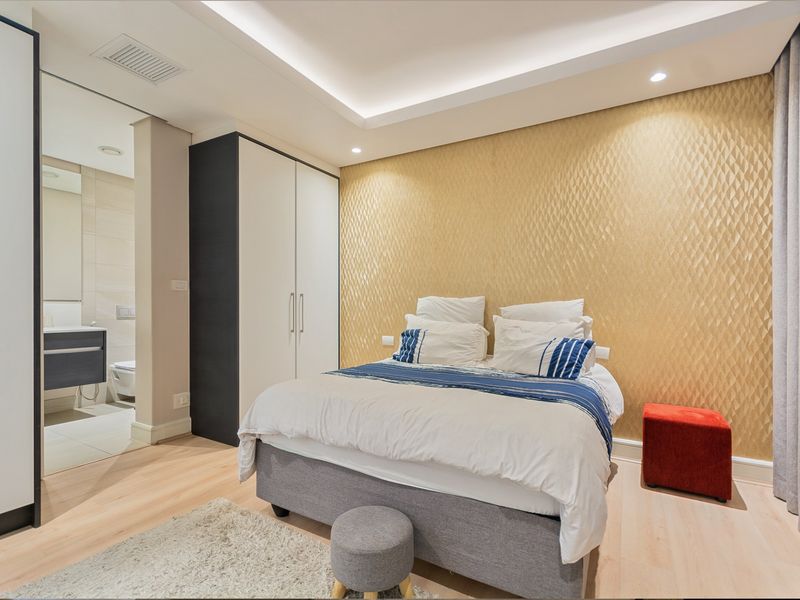 Modern bedroom featuring a textured gold feature wall, built-in wardrobe, recessed ceiling lighting, and direct access to an en-suite bathroom.