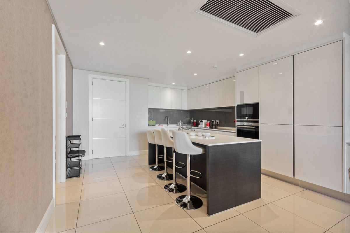Modern kitchen featuring high-gloss cabinetry, a central island with breakfast bar seating, built-in appliances, and sleek tiled flooring.
