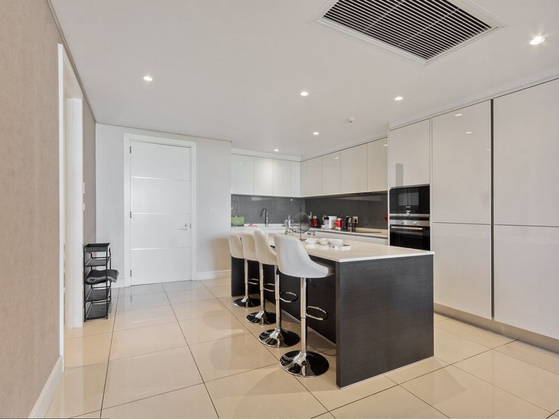 Modern kitchen featuring high-gloss cabinetry, a central island with breakfast bar seating, built-in appliances, and sleek tiled flooring.