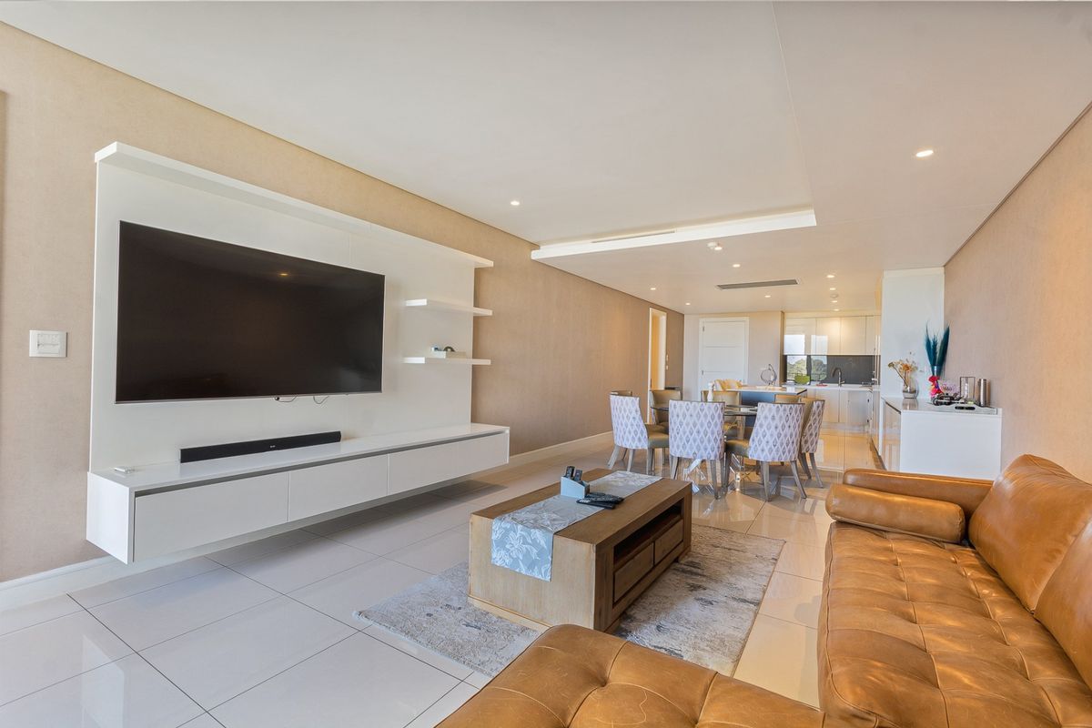 Spacious open-plan living and dining area featuring modern tiled floors, recessed lighting, and a sleek built-in media wall, flowing into a contemporary kitchen.