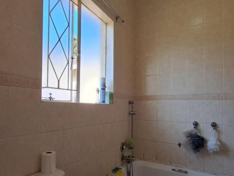 A functional bathroom featuring tiled walls, a bathtub with a shower mixer, and a window with security bars.