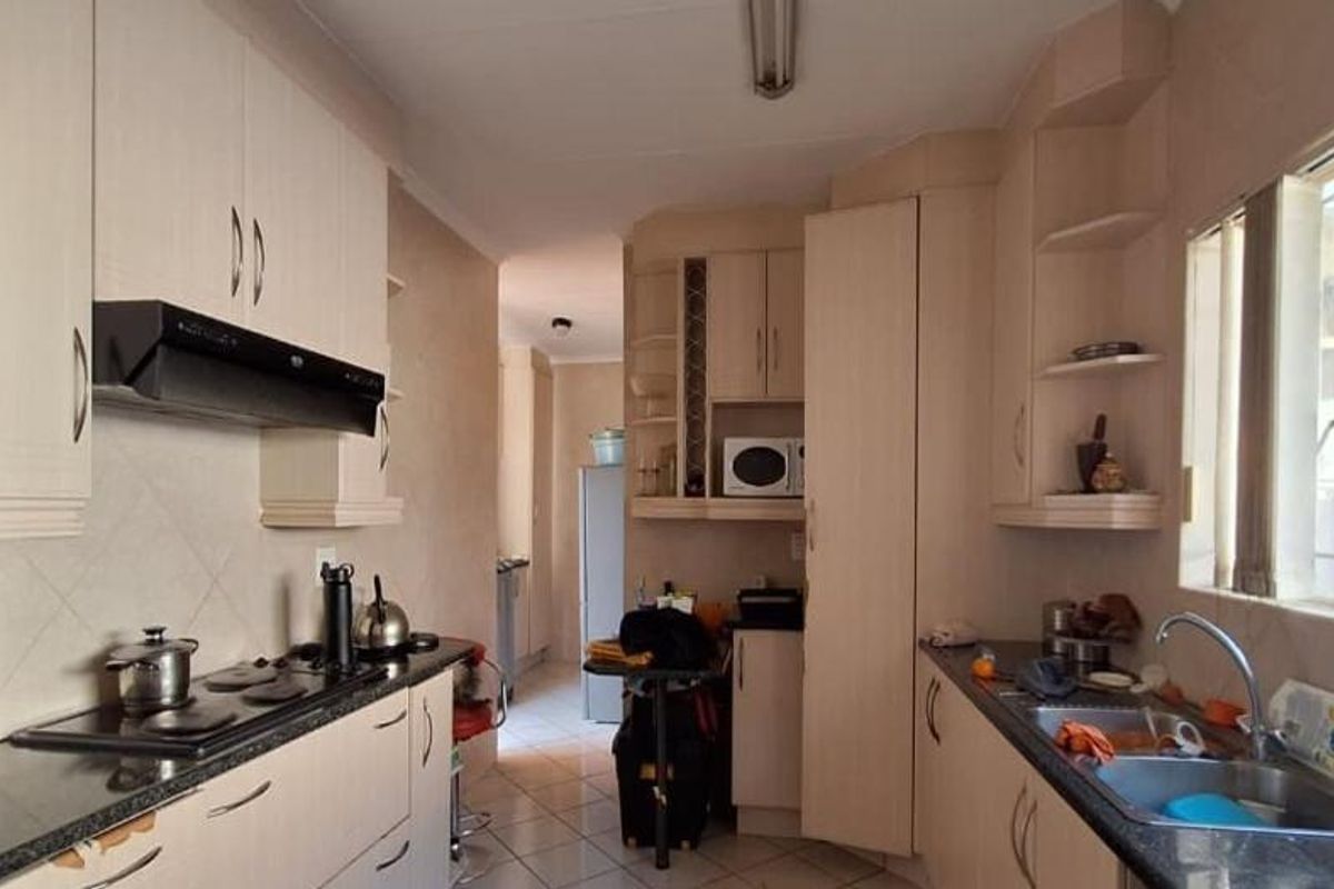 A functional kitchen featuring light-toned built-in cabinetry, granite countertops, an electric hob with extractor, and a double sink with natural light.