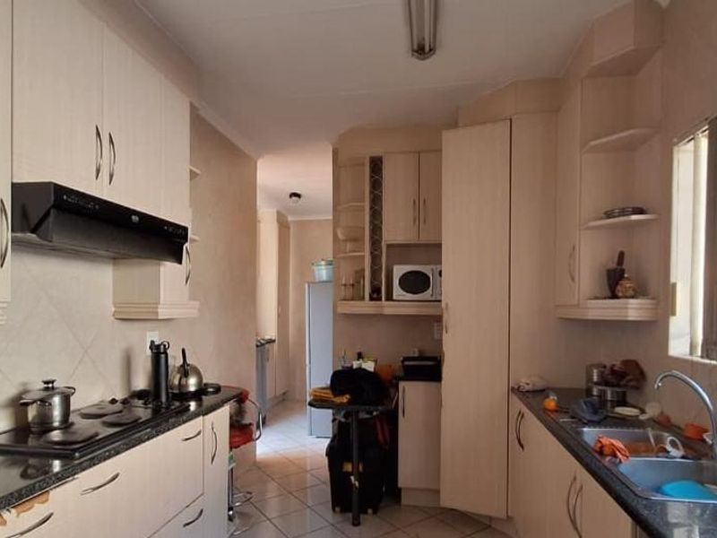 A functional kitchen featuring light-toned built-in cabinetry, granite countertops, an electric hob with extractor, and a double sink with natural light.