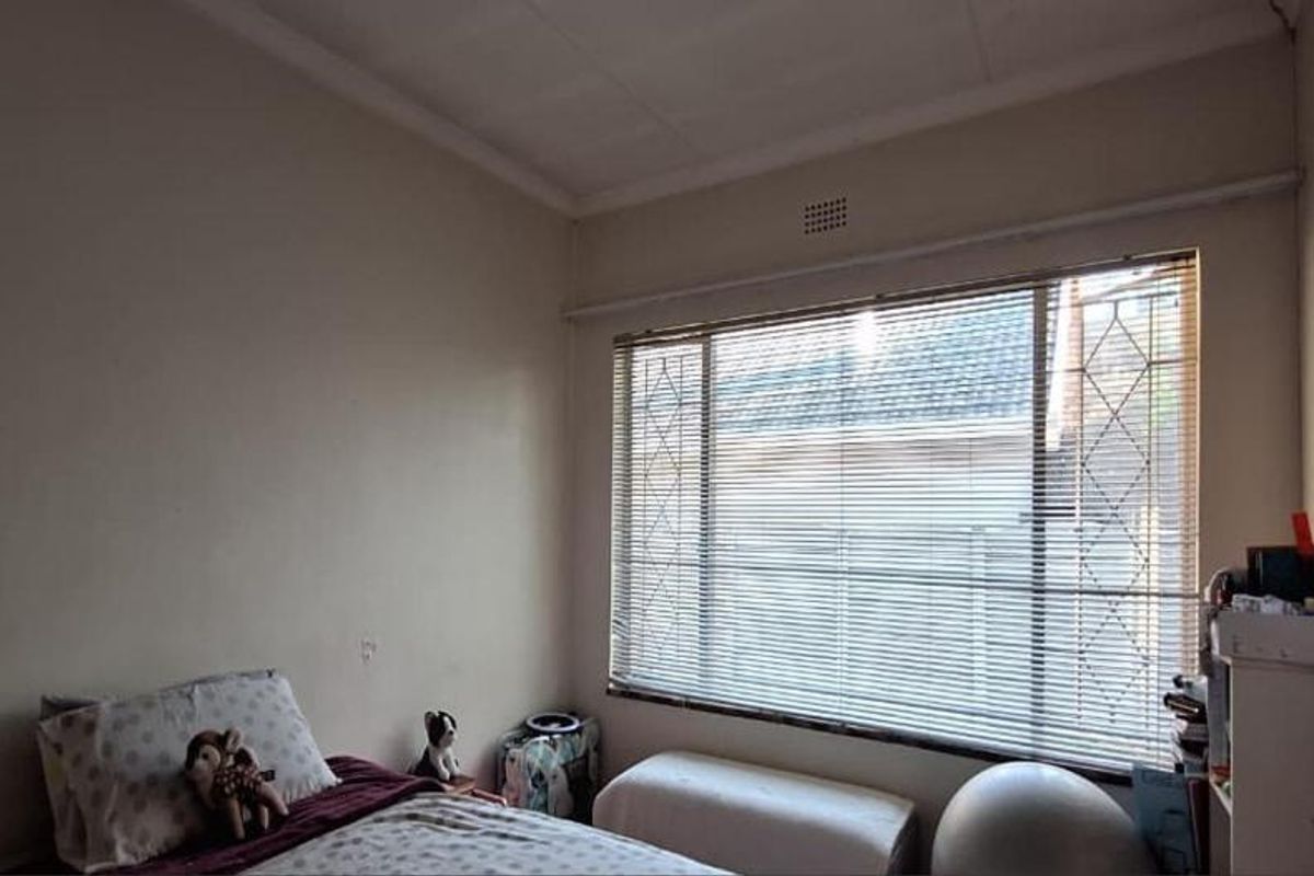 A bedroom featuring a large window with security bars and venetian blinds, requiring cosmetic updates to the wall finishes.
