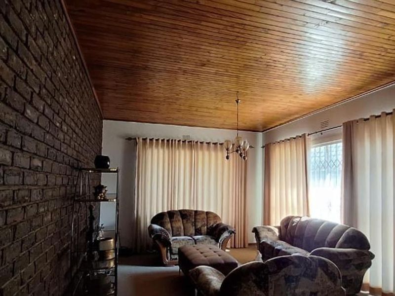 Spacious living room featuring a distinctive exposed brick feature wall and a warm timber tongue and groove ceiling.