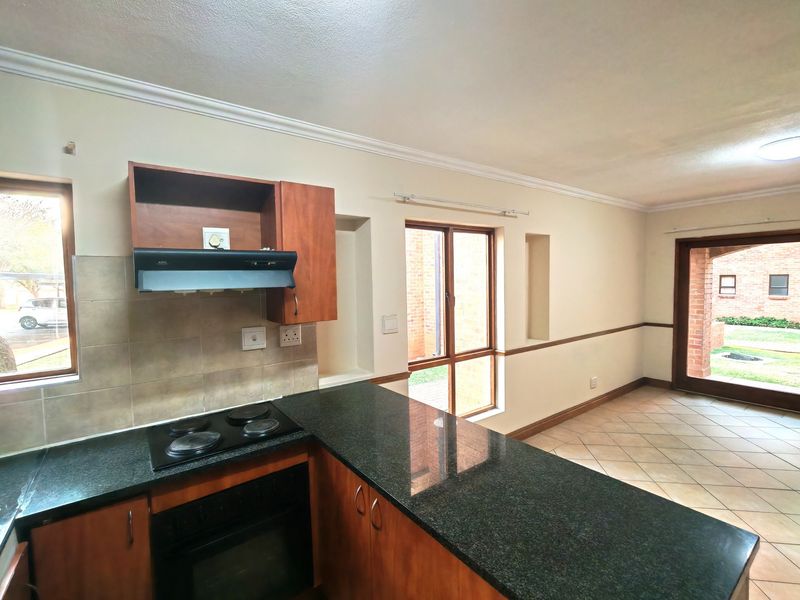 Open-plan kitchen and living area featuring dark granite countertops, wooden cabinetry, electric hob, and tiled flooring with direct access to the exterior.