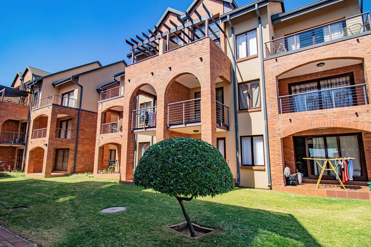 Rear view of a multi-story apartment complex featuring exposed brick architecture, arched balconies with metal railings, and a well-maintained communal lawn area.