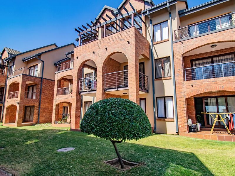 Rear view of a multi-story apartment complex featuring exposed brick architecture, arched balconies with metal railings, and a well-maintained communal lawn area.