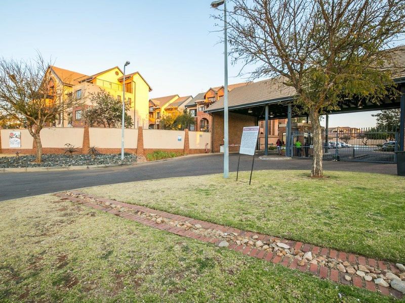 The entrance to the Hill Top apartment complex featuring a secure gated access point, perimeter walling, and well-maintained landscaped grounds.