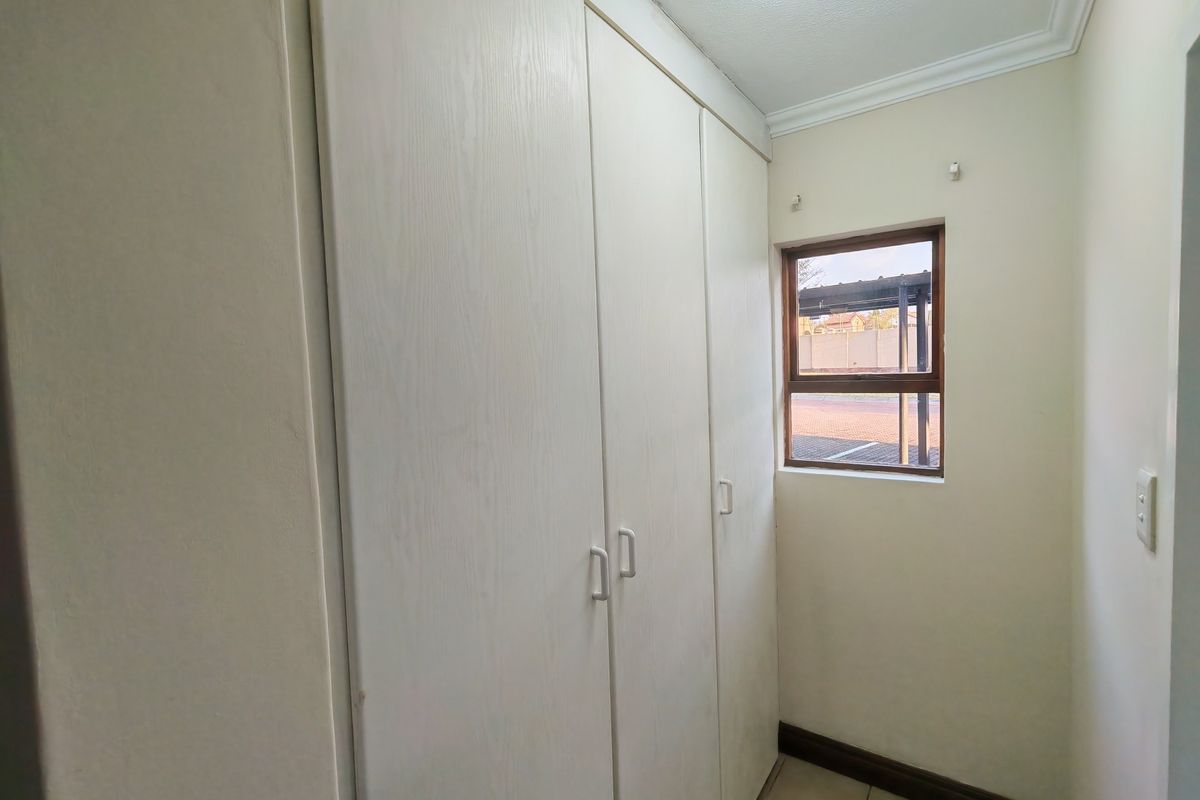 A clean, empty bedroom featuring built-in cupboards, tiled flooring, and a window providing natural light.
