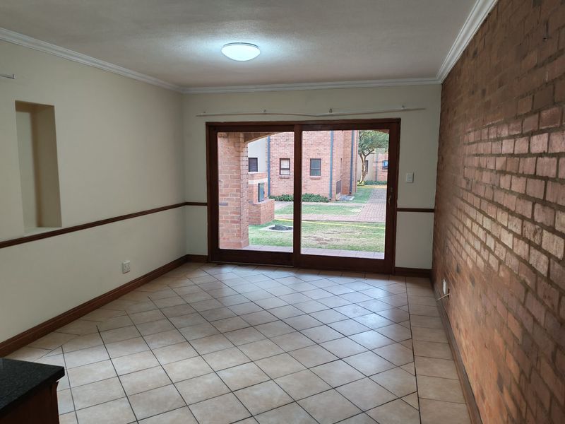 An empty living room featuring an exposed brick feature wall, tiled flooring, and a sliding glass door providing access to the exterior.